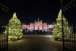 View of Blenheim palace lit up at Christmas through the gates and two Christmas trees