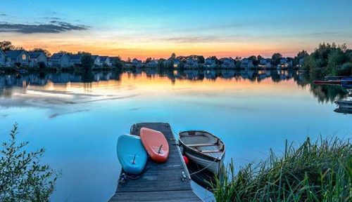 Paddleboards and a boat tied to the jetty at Meadowlark on Summer lake at sunset